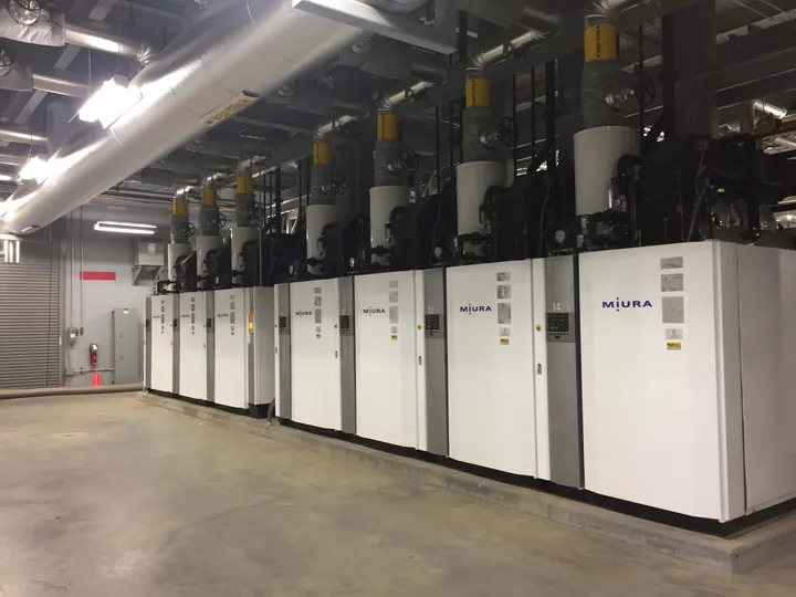 Row of Miura modular steam boilers with insulated overhead steam headers in a commercial boiler room