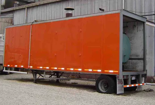 Orange enclosed mobile boiler room trailer set up alongside a plant building