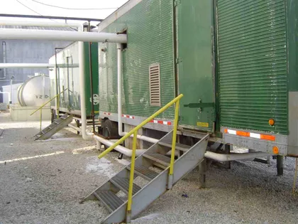 Two green mobile boiler-room trailers with access stairs tied into plant steam piping