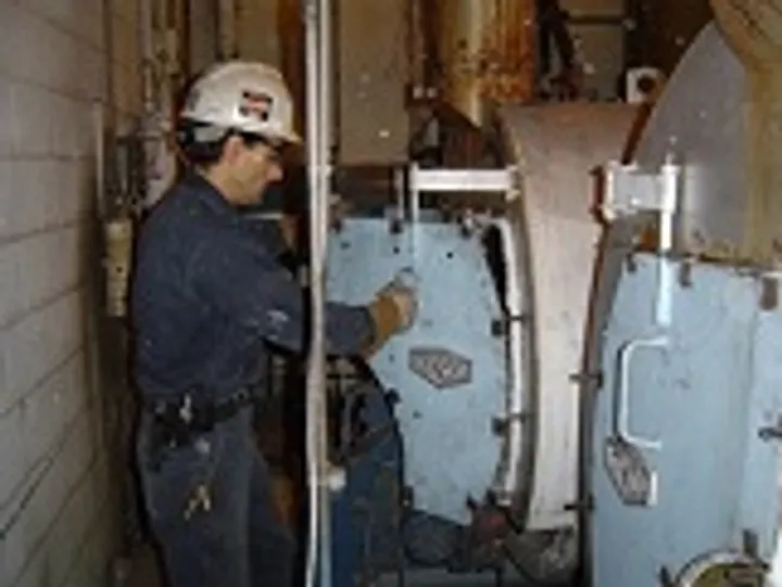 D. B. Johnsen technician in a hard hat working on an opened boiler front during a service call